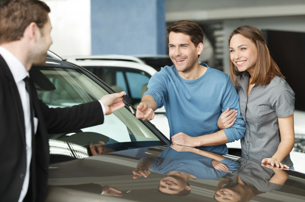 car dealership personnel handing keys to a couple