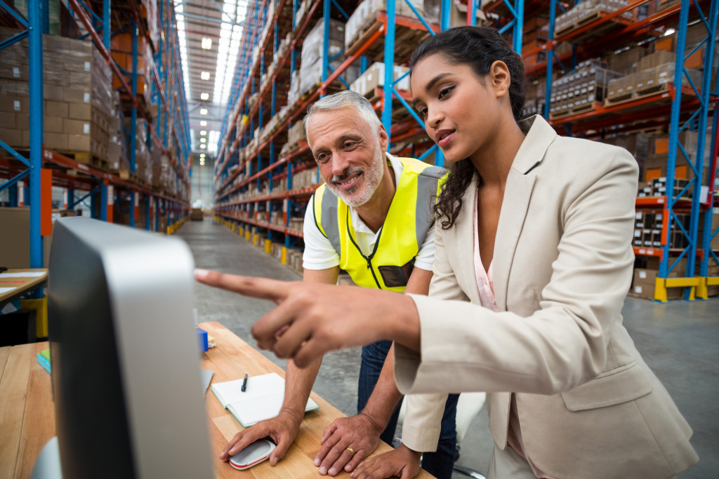 a female businesswoman and warehouse personnel looking at a computer